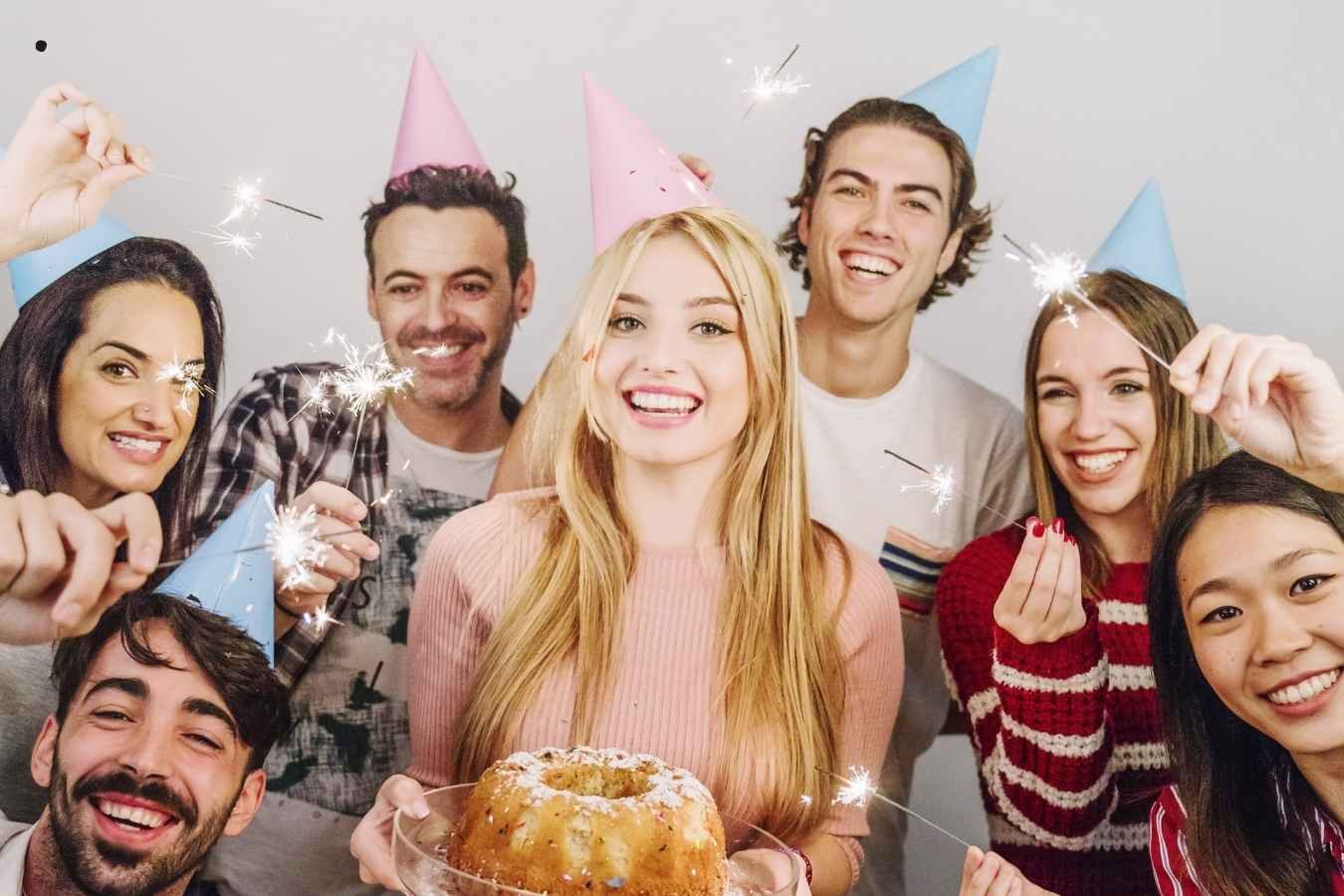 A joyful birthday celebration scene where a man presents a birthday cake with candles to his girlfriend surrounded by friends. Everyone is smiling, holding drinks, and enjoying the moment in a warmly lit room, embodying the essence of heartfelt birthday wishes for a girlfriend.