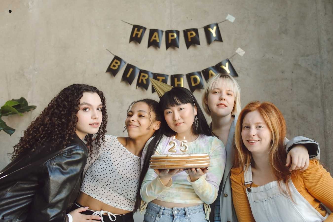 A joyful birthday celebration scene where a man presents a birthday cake with candles to his girlfriend surrounded by friends. Everyone is smiling, holding drinks, and enjoying the moment in a warmly lit room, embodying the essence of heartfelt birthday wishes for a girlfriend.