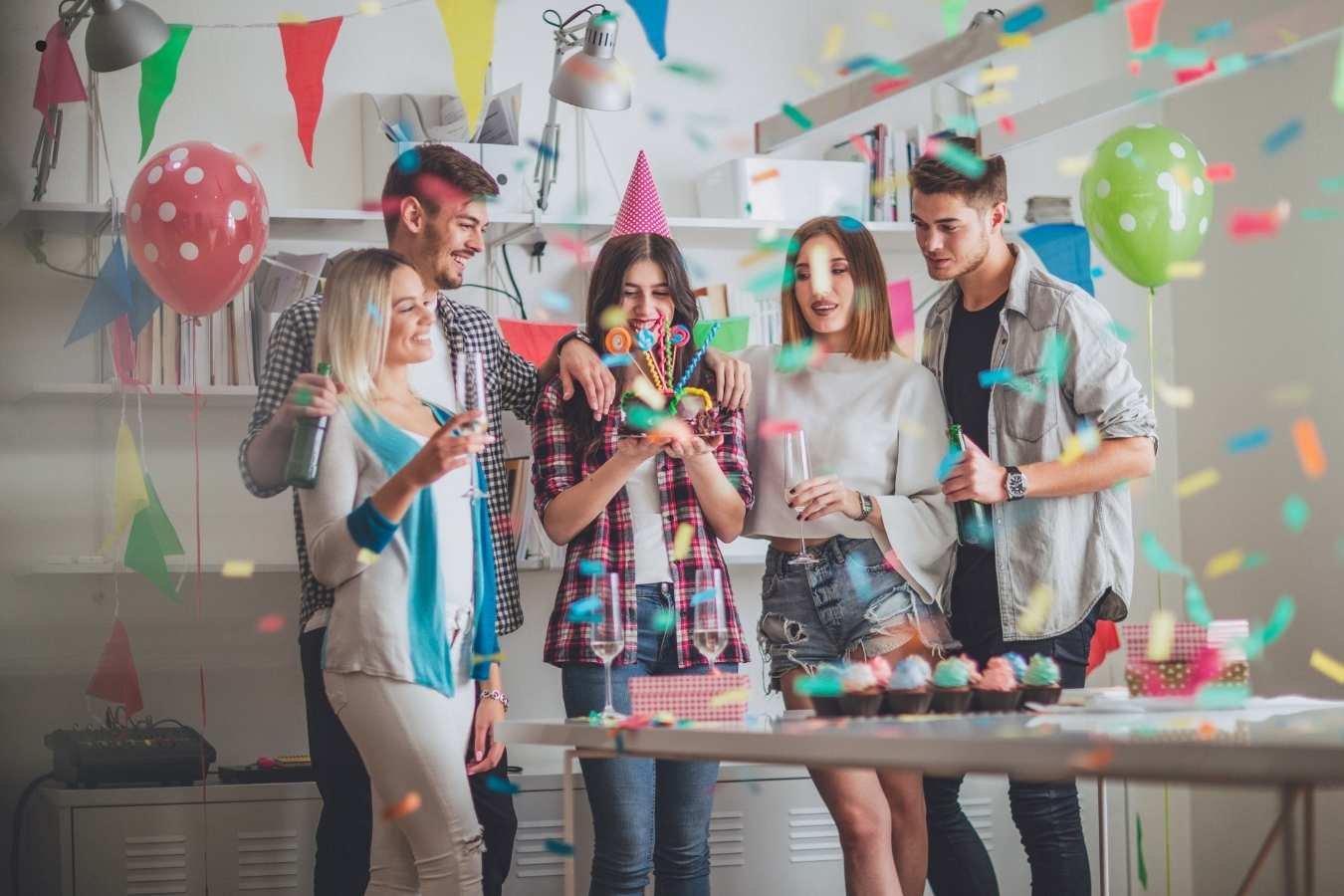 A joyful birthday celebration scene where a man presents a birthday cake with candles to his girlfriend surrounded by friends. Everyone is smiling, holding drinks, and enjoying the moment in a warmly lit room, embodying the essence of heartfelt birthday wishes for a girlfriend.