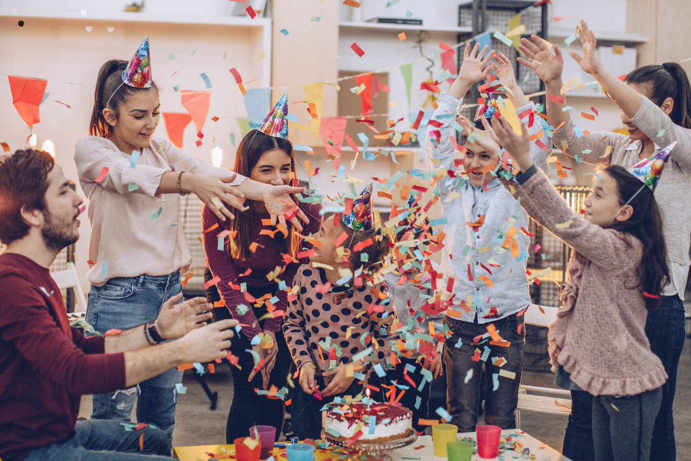 A joyful birthday celebration scene where a man presents a birthday cake with candles to his girlfriend surrounded by friends. Everyone is smiling, holding drinks, and enjoying the moment in a warmly lit room, embodying the essence of heartfelt birthday wishes for a girlfriend.